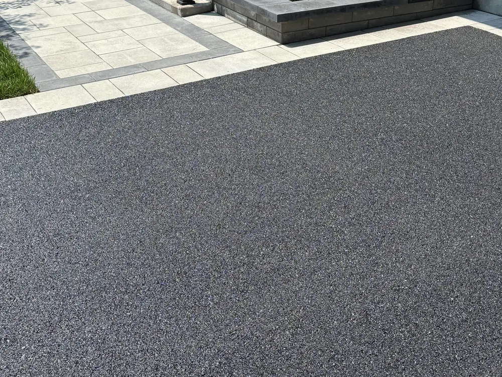 Entrée d'asphalte bordée de pavé uni pâle devant une résidence