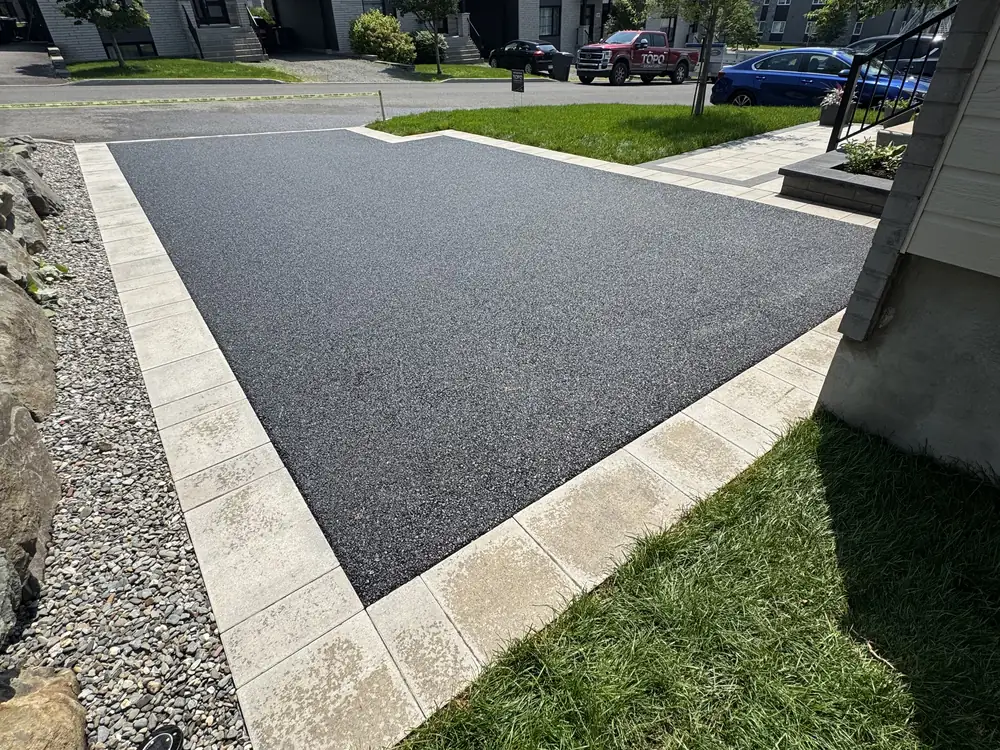 Entrée d'asphalte encadrée d'une bordure de pavé uni pâle